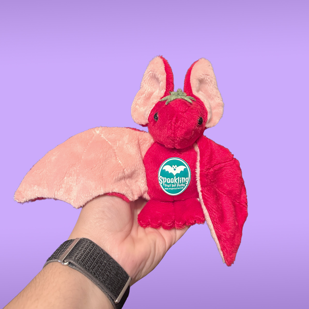 Red plush bat toy with a visible brand logo held against a purple background