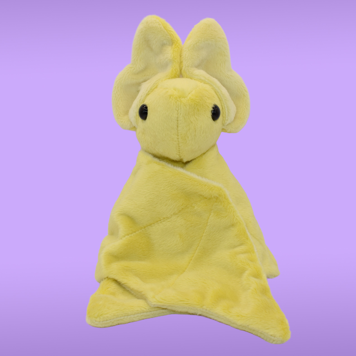 Yellow Spookling bat plush with light yellow ears against a Lavander background, shown with wings closed