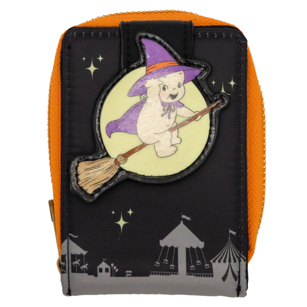 A small zippered pouch with an orange side and zipper, a black front panel, and a Halloween-themed patch showing a cartoon baby character in a purple witch hat riding a broomstick on a pale yellow moon. The front also has black star graphics and gray circus tent silhouettes near the bottom.