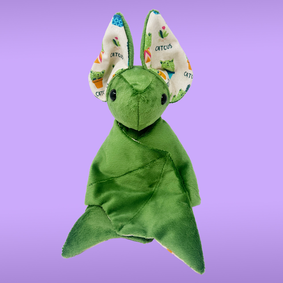 Green plush toy with colorful cactus-patterned ears on a purple background