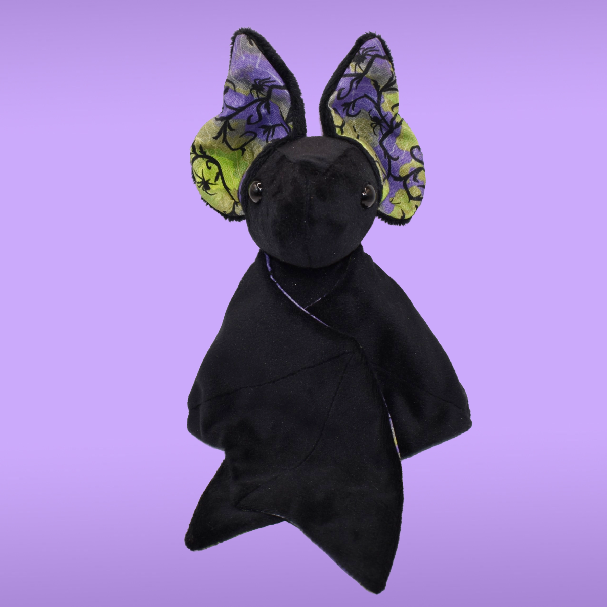 Black Spookling bat plush with neon green and purple spiderweb print ears against a lavender background, shown with folded wings