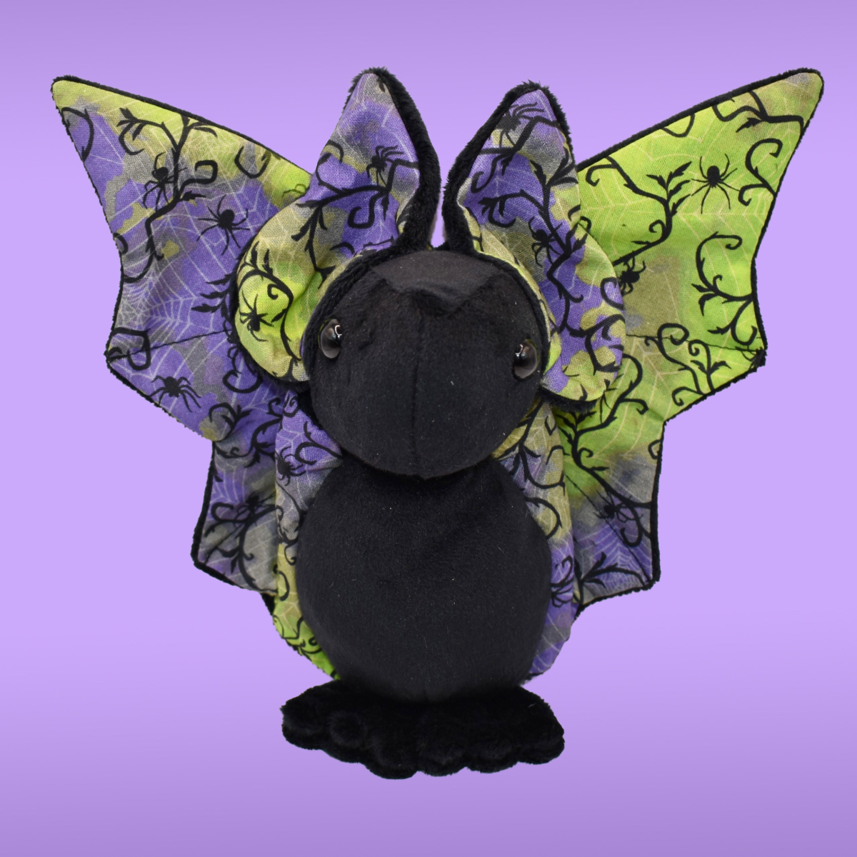 Black Spookling bat plush with fully open neon spiderweb print wings displayed on a lavender background