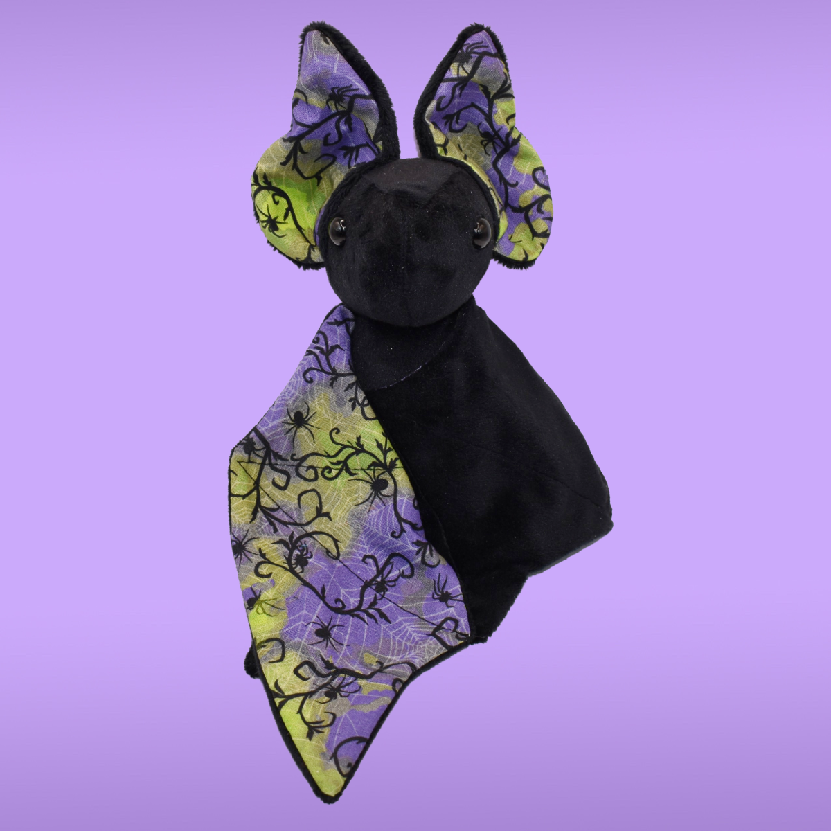 Black Spookling bat plush with neon spiderweb print wings featuring spiders and web details in purple and green tones