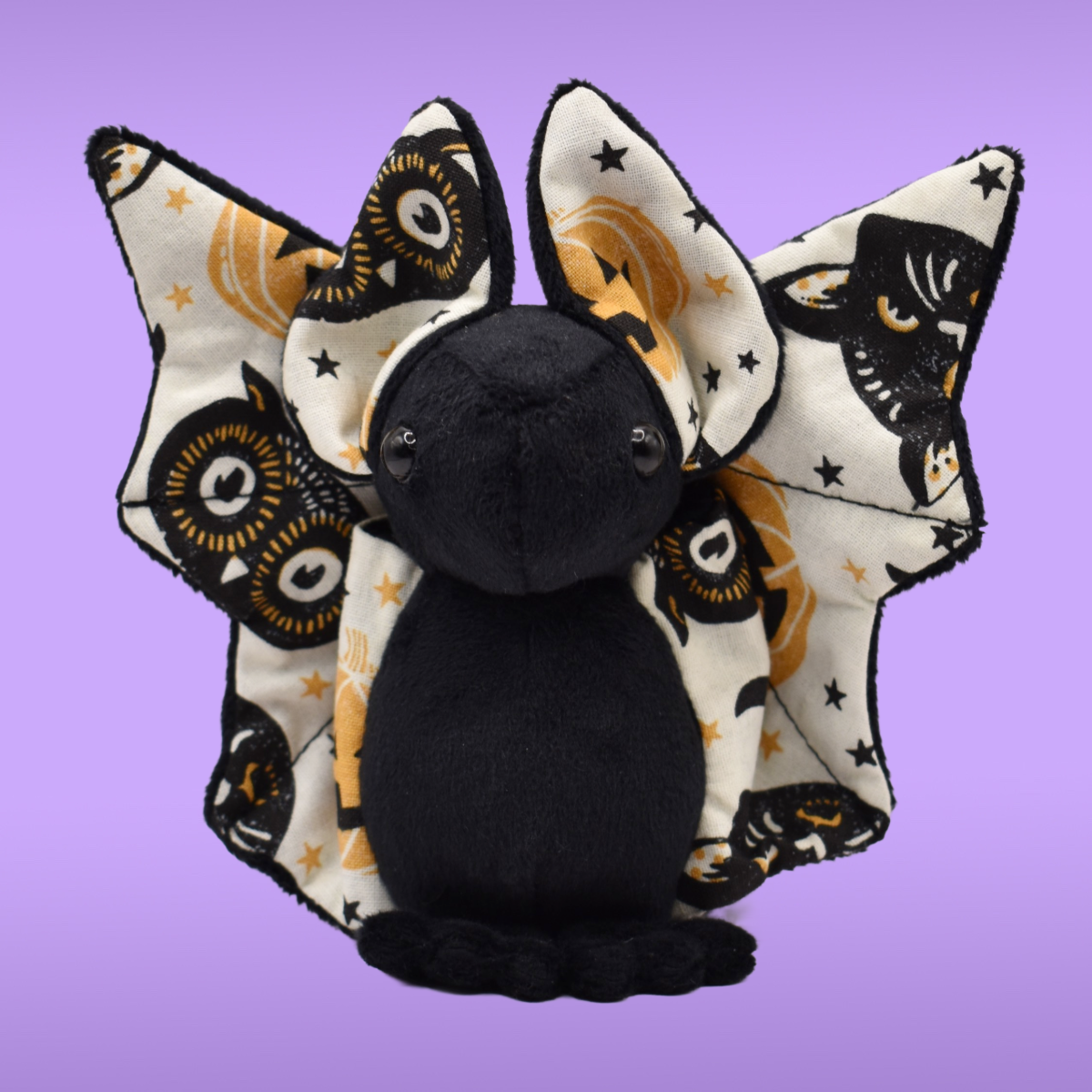  Black Spookling bat plush with fully open vintage Halloween print wings displayed on a lavender background