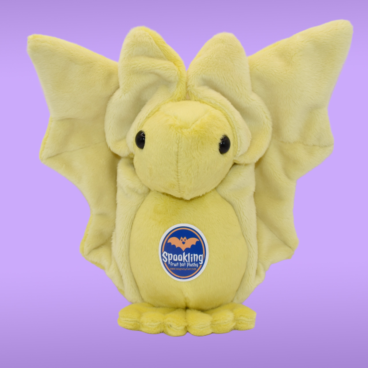 yellow Spookling bat plush with fully open
light yellow print wings displayed on a lavender background 